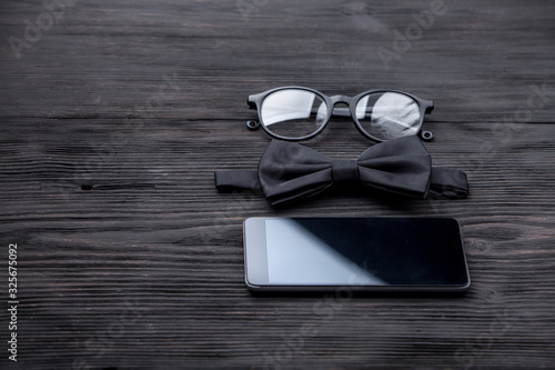 Stylish hipster fashion concept in minimal style. Trendy eyewear, bow tie black wooden grunge table photo