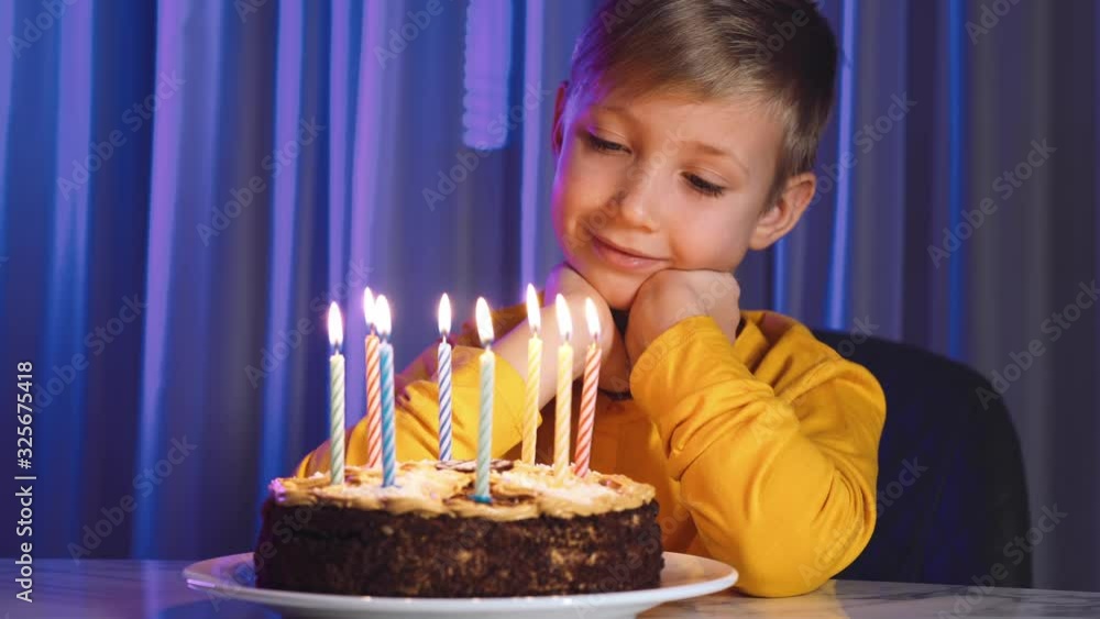 Cute boy blows out candles on a cake on his birthday. Happy child looks at a cake with candles. Child looks at the cake and makes a birthday wish. Boy celebrates his birthday. Happiness concept Cute boy blows out candles on a cake on his birthday. Happy child looks at a cake with candles. Child looks at the cake and makes a birthday wish. Boy celebrates his birthday. Happiness concept