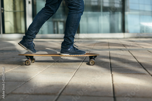 Man skateboarding in city with one foot placed on board and pushing off with the other. Riding on longboard on paving stone. Selective focus on skateboard. Concept of leisure activity and urban.