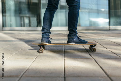 Stylish skateboarder in jeans and sneakers riding on longboard. Outdoor riding on skateboard on paving stone. Selective focus on hipster. Concept of leisure activity and urban. Side view.