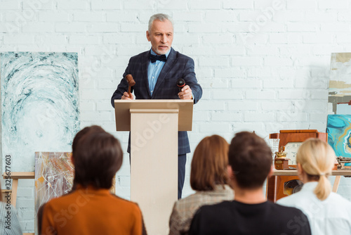 Photography selective focus of auctioneer holding gavel and microphone and looking at buyers