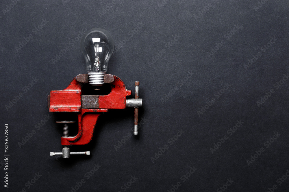 Light bulb clamped in mechanical hand vise on grey background with copy-space. Creative concept