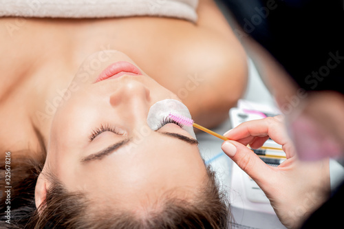 Cosmetologist hand making lengthening lashes with eyelash brush, close up.