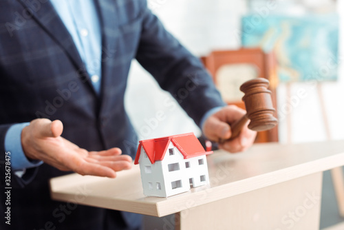 cropped view of auctioneer pointing with hand at model of house and holding gavel during auction