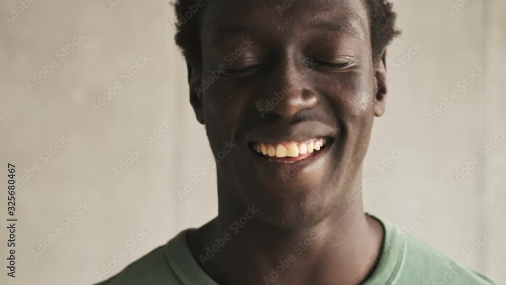A close-up view of a positive handsome young african american man is laughing to the camera in the light living room