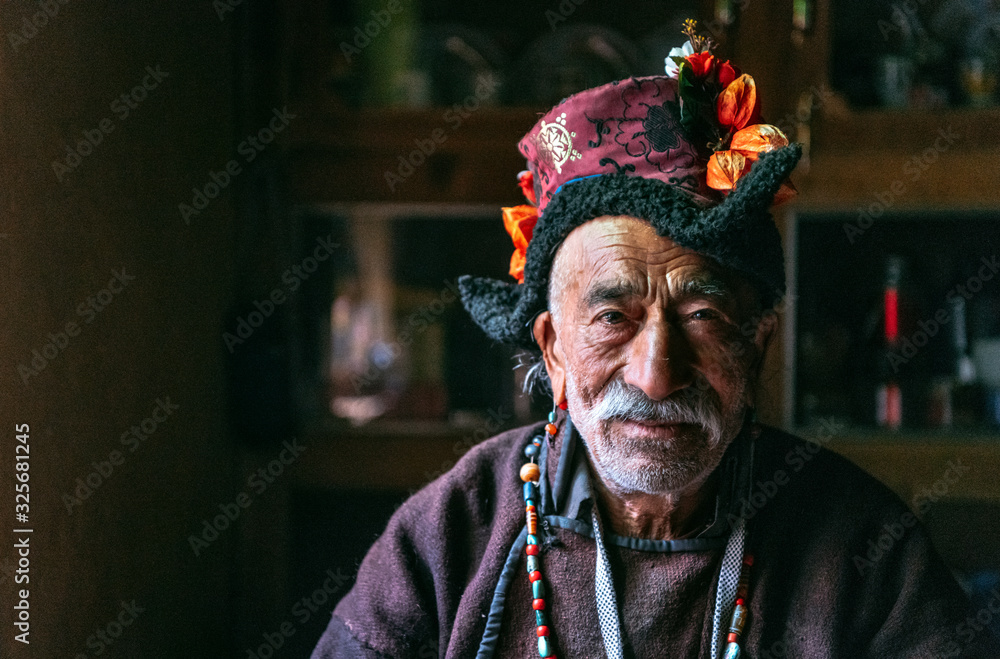 Portrait of an old man in typical tibetan clothes inside his house in Ladakh, Kashmir, India.