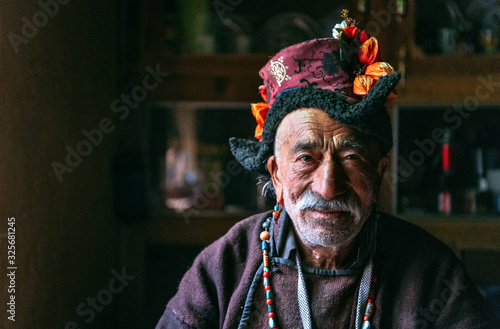 Portrait of an old man in typical tibetan clothes inside his house in Ladakh, Kashmir, India.