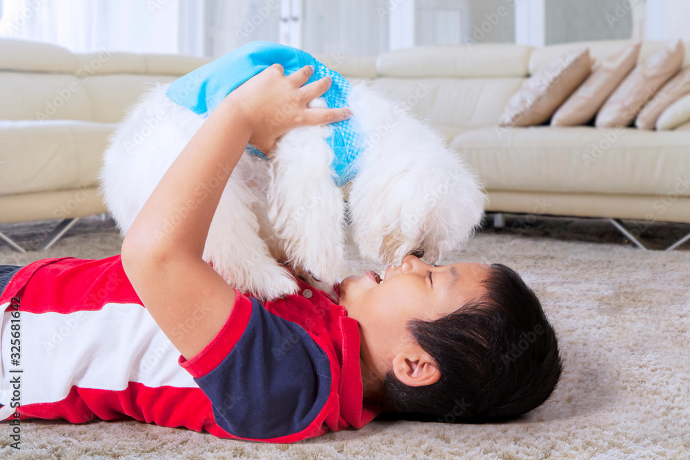Obraz premium Boy rubbing nose with his white dog in his home