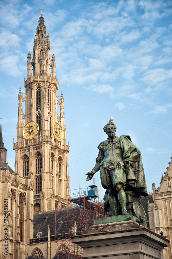 Vertical view of bell tower of Cathedral of Our Lady in Antwerp, UNESCO world heritage site in Belgium with statue of Pieter Paul Rubens with pigeon on his head in front. Travel tourism in Benelux.