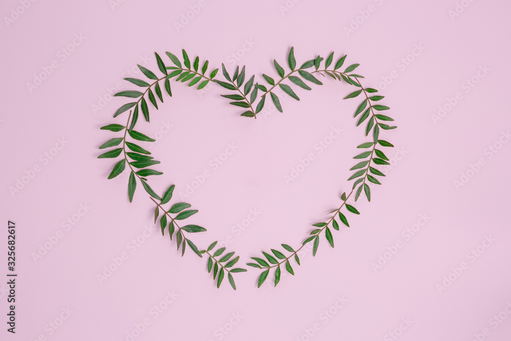 Heart composition from green leaves on a pink background. Flat lay, top view Heart composition from green leaves on a pink background. Flat lay, top view