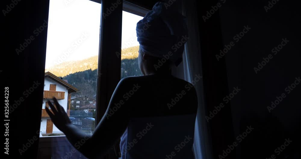 A woman looks at the setting sun with a towel on her head after a shower on a terrace overlooking the mountains. A woman looks at the setting sun with a towel on her head after a shower on a terrace overlooking the mountains.