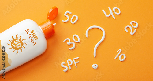 Sunscreen on orange background. Plastic bottle of sun protection and white cream in the form of question mark and numbers SPF. How to choose a sunscreen photo