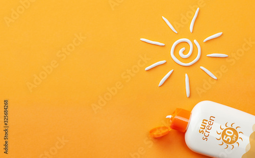Sunscreen on orange background. Plastic bottle of sun protection and white sun-shaped cream photo