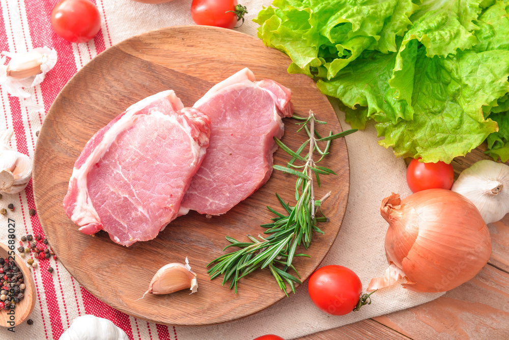 Plate with raw pork meat and vegetables on wooden background