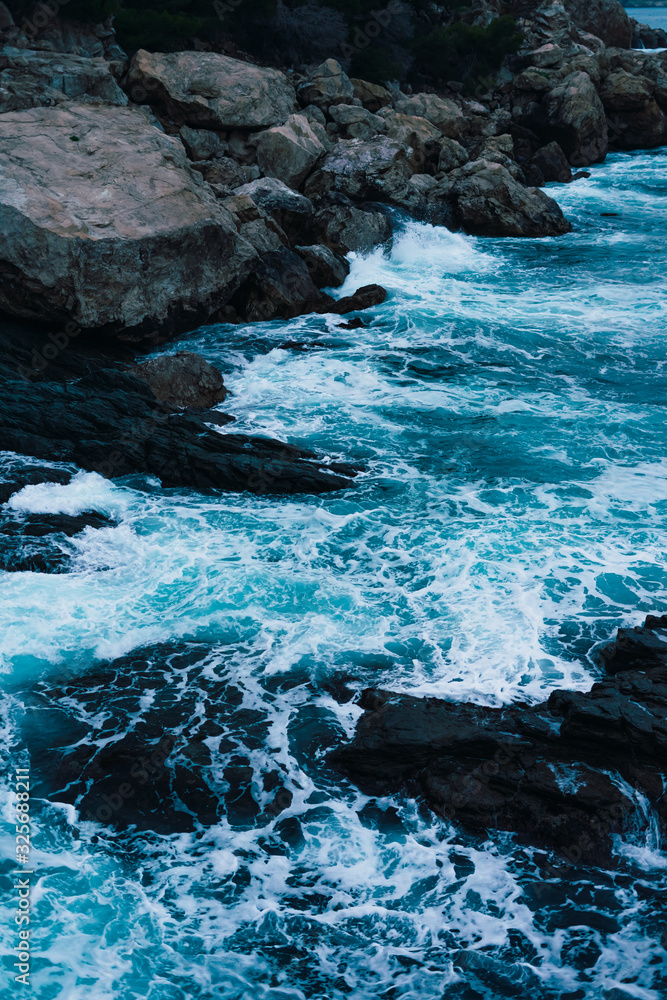 Blue waves of the Mediterranean sea reaching the coast breaking against the rocks and creating sparkling white areas Blue waves of the Mediterranean sea reaching the coast breaking against the rocks and creating sparkling white areas