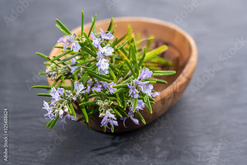 Fresh purple blooming rosemary twigs in an olive wood bowl on a black slate background