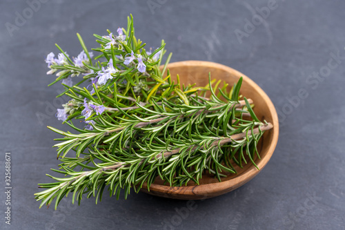 Purple blooming rosemary and fresh rosemary twigs in an olive wood bowl on a black slate background