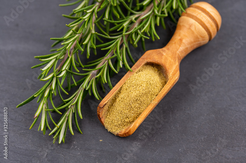 Fresh rosemary twigs and a spice shovel with ground rosemary on a black slate background