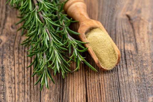 Fresh rosemary twigs and a small wooden spice shovel with ground rosemary on a rustic wooden background