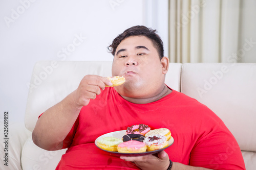 Fotografie Fat man chewing doughnuts in his living room
