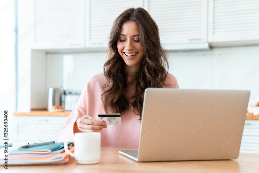 Woman sit indoors at home using laptop holding credit card. Woman sit indoors at home using laptop holding credit card.