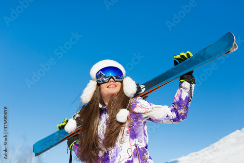 Winter portrait of a young sporty woman with a ski on a mountain peak over sky background.