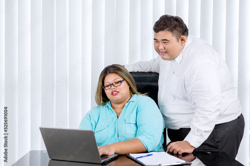 Fat man supervising her female worker working Fat man supervising her female worker working