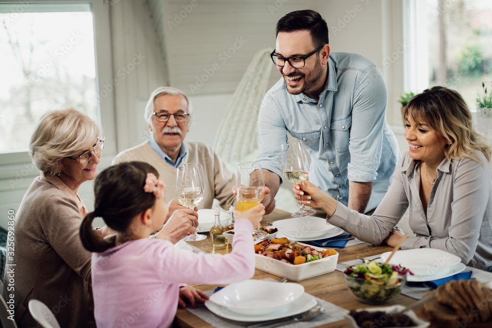 Happy mid adult man toasting with his family during lunch at dining table.