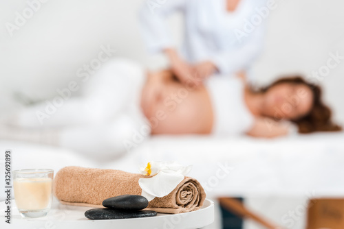 Selective focus of stones  candle with orchid on table and masseur doing massage to pregnant woman on massage table in spa center