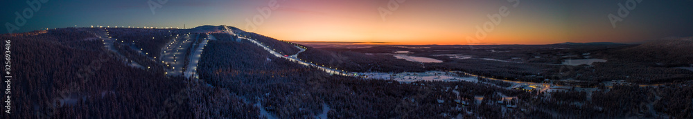 A panoramic drone shot of the ski slopes of Levi ski resort at sunrise, Kittilä, Finland. A wintery landscape in Finnish Lapland. 