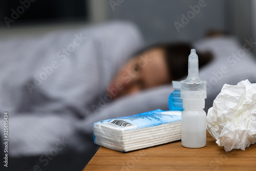 Woman with a cold lying in bed at home trying to cure herself. Nasal spray and tissue used for running nose, sinusitis
