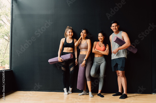 Happy smiling man and women looking at camera altogether in gym. Group of young people relaxing in gym after workout training with black background.