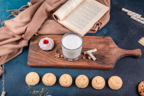 Vanilla meringue cake with butter and oatmeal cookiesand a glass of milk on a wooden board on a blue table