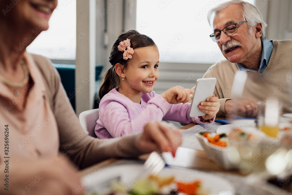 Cute little girl using mobile phone while having lunch with grandparents at dining table. Cute little girl using mobile phone while having lunch with grandparents at dining table.