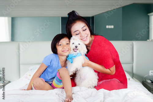 Woman and girl hugging their dog in the bedroom