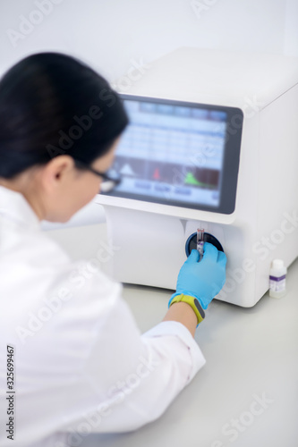 Technician in blue gloves pressing the start button of hematological analyzer
