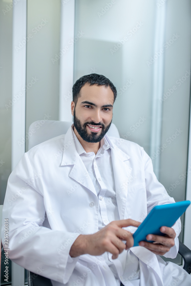Male doctor in a white robe sitting in the chair and searfing internet Male doctor in a white robe sitting in the chair and searfing internet
