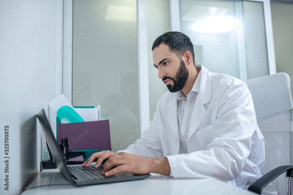 Male doctor in a white robe typing a message Male doctor in a white robe typing a message