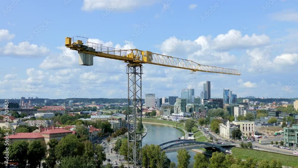 Tower construction crane stands motionless, swaying in the wind on background of aerial city view of Vilnius, Lithuania. Tower construction crane stands motionless, swaying in the wind on background of aerial city view of Vilnius, Lithuania.