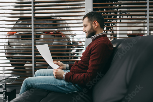 Canvas Print A brunette bearded man sits on a couch and reads a contract in a saloon