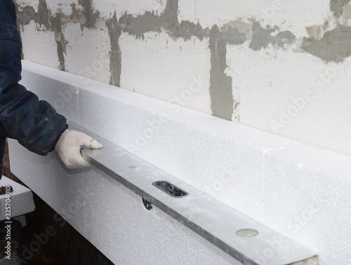 Foto Builder holding spirit level in hand on the rigid styrofoam insulation wall