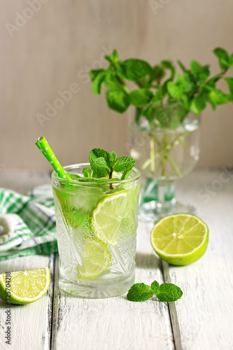 Mojito. Refreshing cold drink with lime and mint in a glass on a white wooden board table. Selective focus, copy space