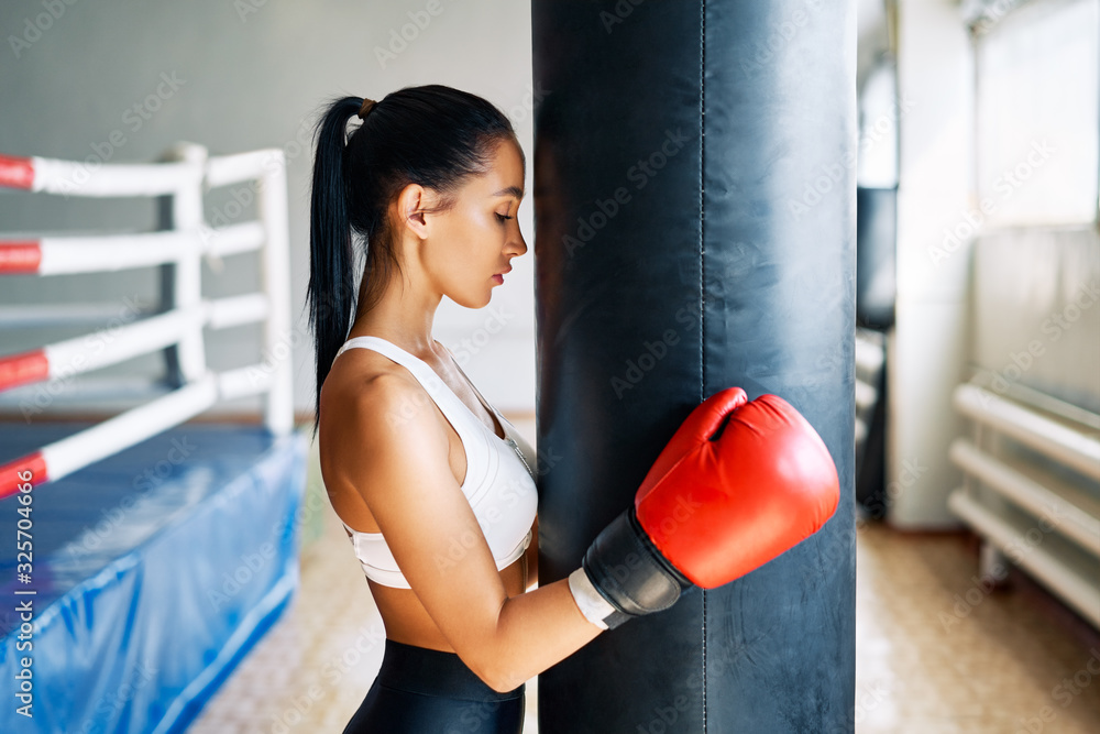 Sporty young woman wearing boxing gloves posing in gym