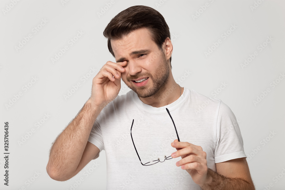 Unhealthy young man dropping glasses, rubbing eyes head shot. Unhealthy young man dropping glasses, rubbing eyes head shot.