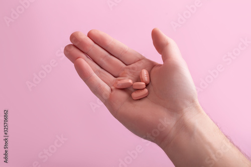 Men holding hiv therapy pills on pink background.