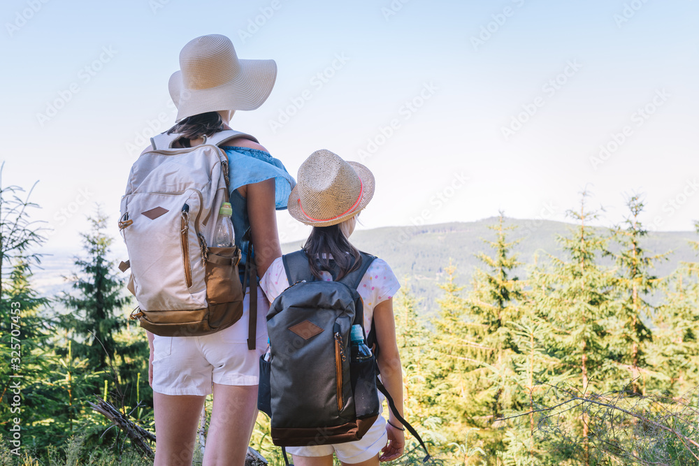 Two sisters travelers with backpacks on the mountain trail admire the views