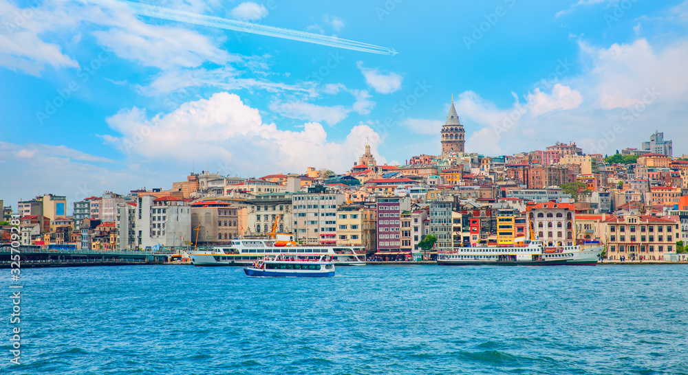Obraz premium Trail of white smoke from the airplane on blue sky - Galata Tower, Galata Bridge, Karakoy district and Golden Horn at bright blue sky - Istanbul, Turkey