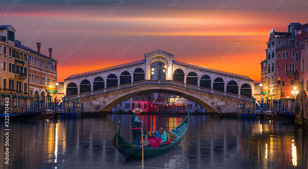 Gondolier carries tourists on gondola Green Canal near Rialto Bridge at sunset - Venice, Italy