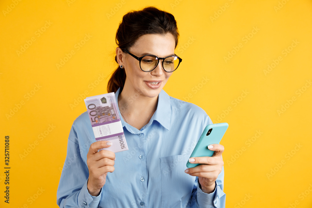 Sale online concept. Stylish businesswoman with money and phone in the yellow studio Sale online concept. Stylish businesswoman with money and phone in the yellow studio