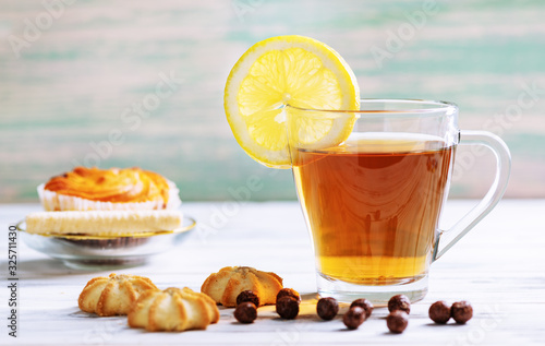 Cup of hot tea with lemon and cookies on a white wooden background.